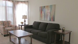 A living room with a sofa, a patterned armchair, a wooden coffee table, and two side tables with lamps.