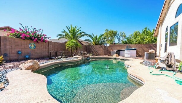 A backyard with a swimming pool, surrounded by a brick wall, palm trees, and a house.