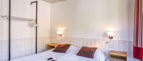 Hotellihuone, jossa on suuri sänky, kaksi yöpöytää, kaksi seinälle kiinnitettyä lamppua, puinen yöpöytä ja punainen verho.