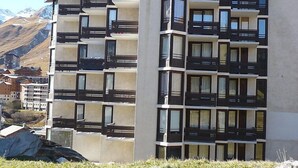 Een meerlaags gebouw met balkons, grote ramen en een bergachtige achtergrond.