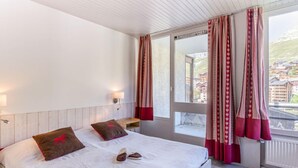 Een slaapkamer met een bed, kussens, een nachtkastje en een raam met gordijnen.
