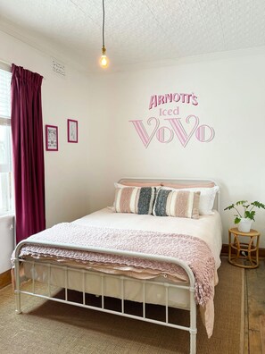 Une chambre à coucher avec un lit, une lampe fixée au mur, une fenêtre avec des rideaux et un panneau décoratif mural.