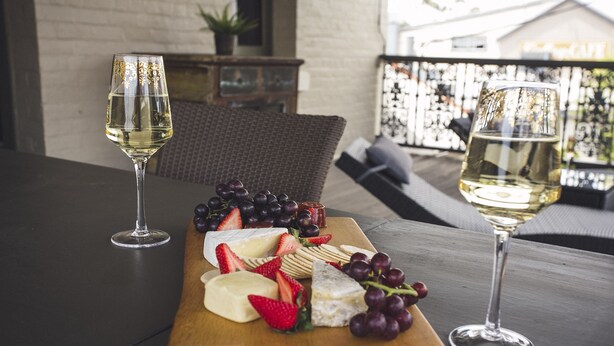 A wooden board with cheese, grapes, and strawberries, accompanied by two glasses of white wine, set on an outdoor table. - William Arnott Boutique Hotel (Morpeth)