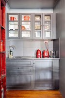 Cocina pequeña con armarios grises, un lavamanos de acero inoxidable y electrodomésticos rojos.