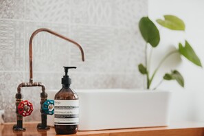 Een badkamer met een witte wastafel, een bruine handzeepfles en een rode en blauwe kraan.