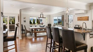 A spacious dining area with a long table and multiple chairs, a kitchen with a granite countertop, and a view of the outdoors. - The BayAway 4 BR Waterview Home in DT Port Orchard (Port Orchard)