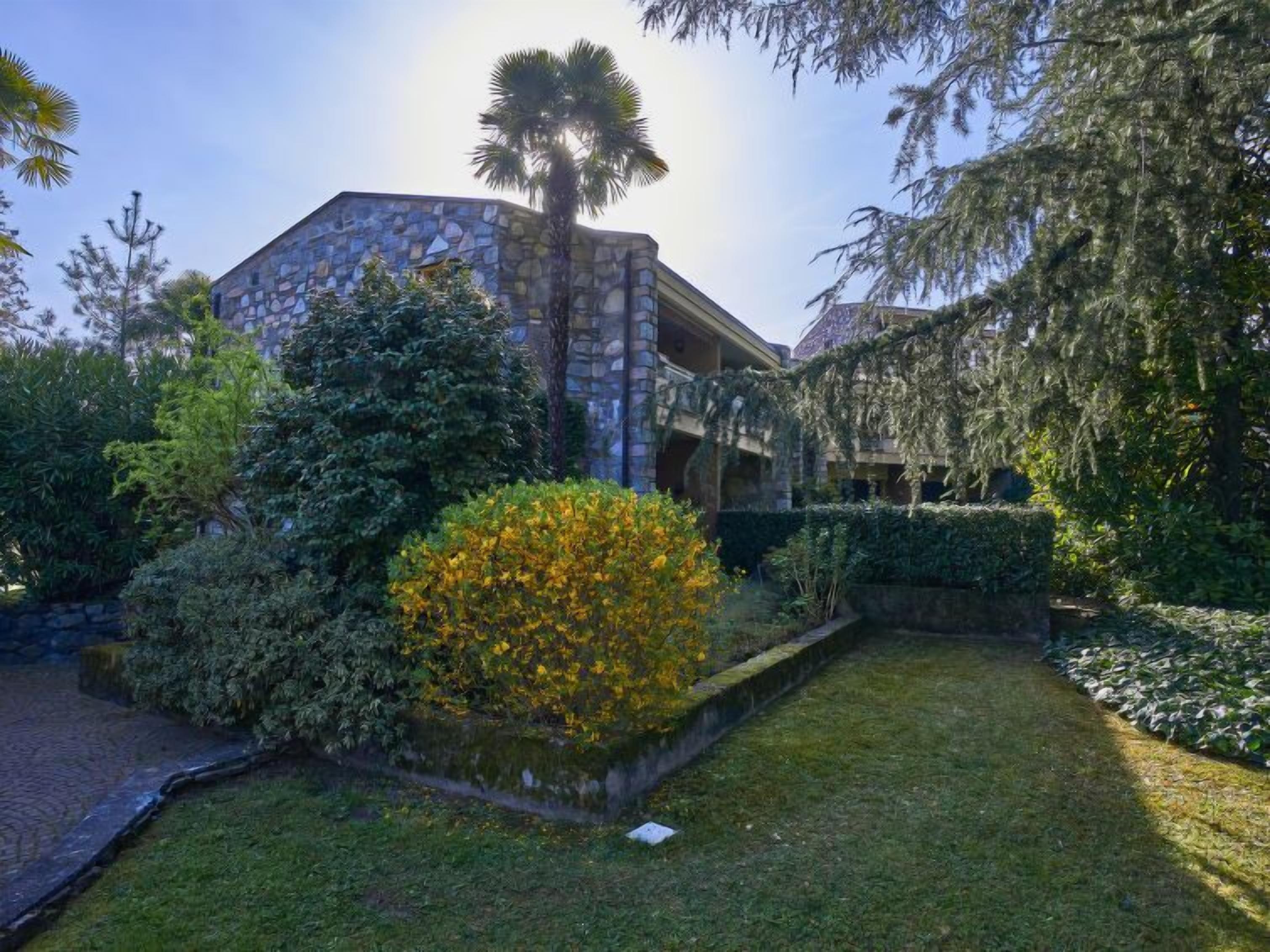 A stone building with a garden in front, including a well-maintained lawn and various shrubs.