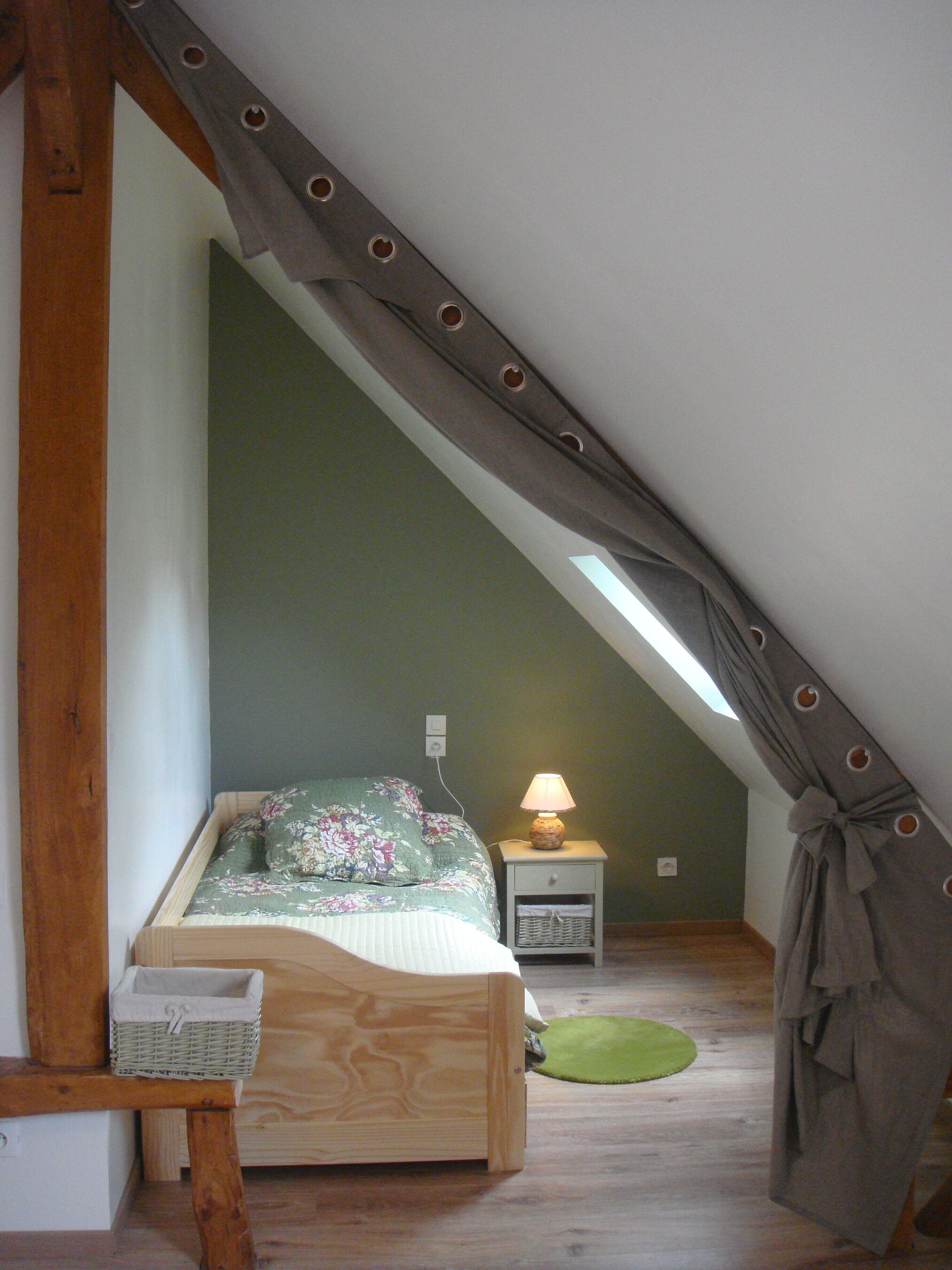 A small, cozy attic bedroom with a sloped ceiling, a wooden bed, a nightstand with a lamp, and a green rug.