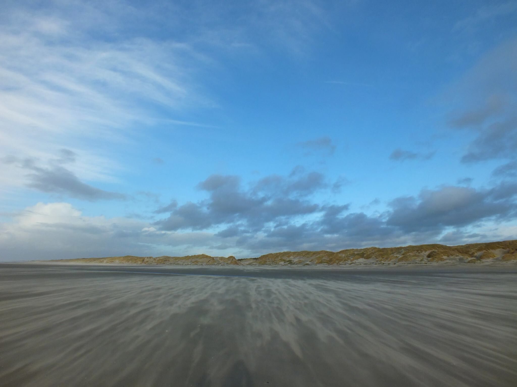 Eine weite, flache Landschaft mit blauem Himmel und sanften Hügeln in der Ferne.