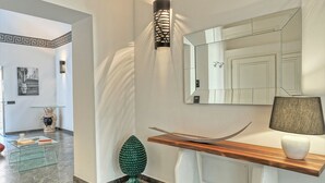 Un interior moderno con una mesa de centro de vidrio, un jarrón verde decorativo, una consola de madera con una lámpara y un espejo grande.