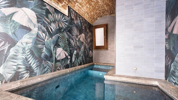 Una piscina con un mural tropical, paredes con azulejos y un ventanal con marco de madera.