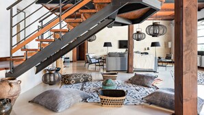 A spacious living area with a wooden staircase, woven baskets, and a cozy seating arrangement. - Splendid Former Chapel With Pool and hot tub (Port Mahon)