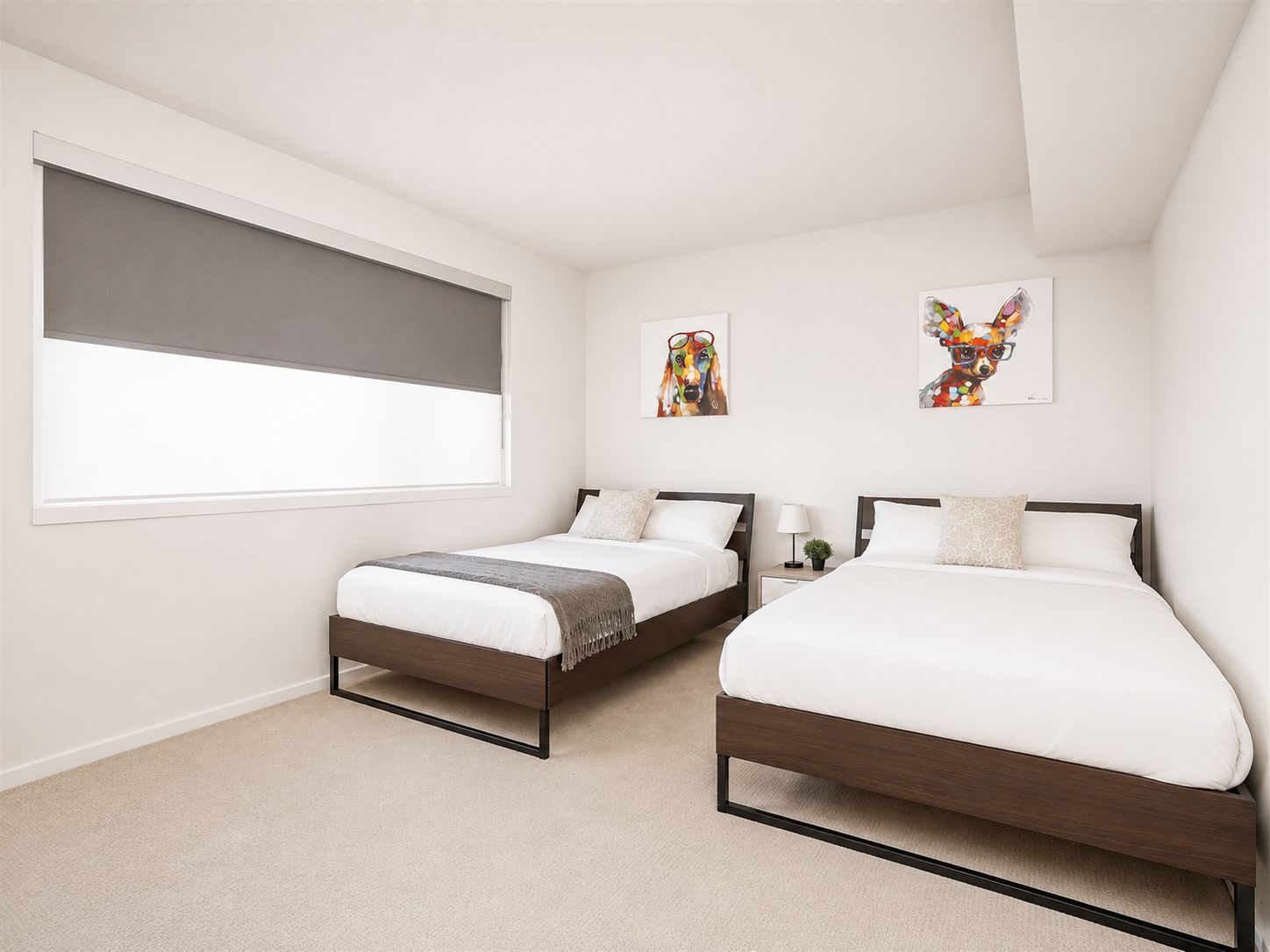 A bedroom with two beds, a window with a blind, and two wall-mounted artworks.