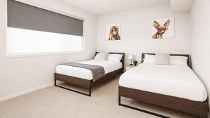 A bedroom with two beds, a window with a blind, and two wall-mounted artworks. - Modern Penthouse on Mass By CozySuites (Indianapolis)