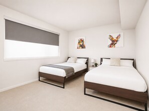 A bedroom with two beds, a window with a blind, and two wall-mounted artworks. - Modern Penthouse on Mass By CozySuites (Indianapolis)