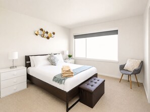 Une chambre à coucher moderne avec un lit, des tables de chevet, un banc, une chaise et une fenêtre.