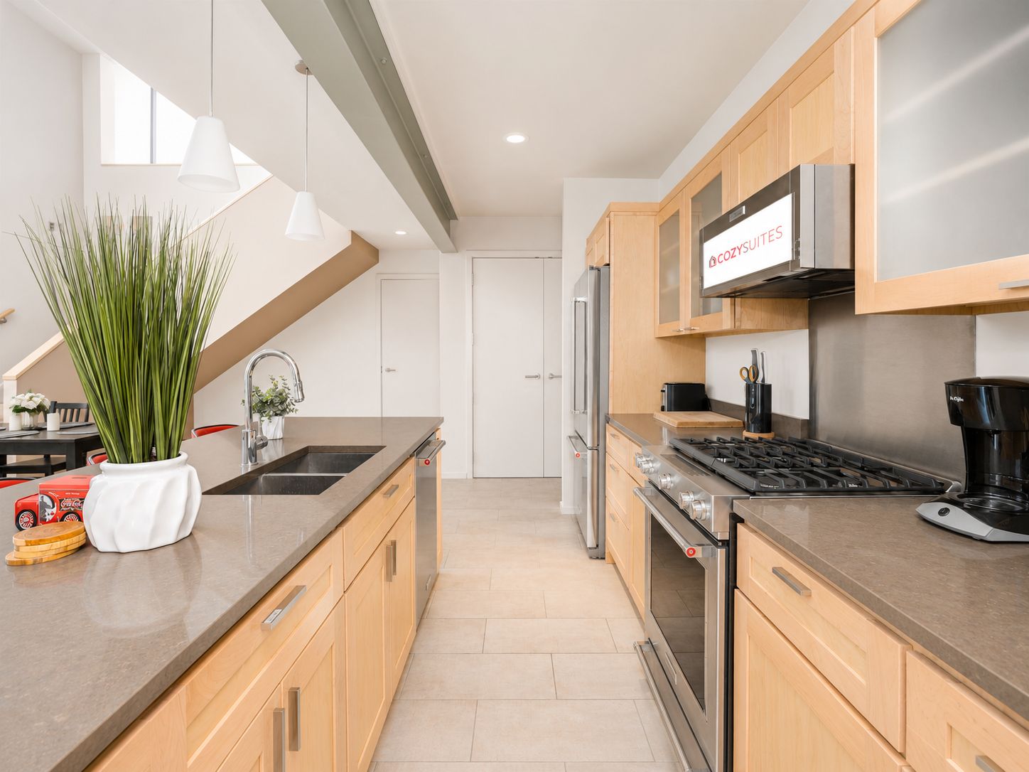 A modern kitchen with stainless steel appliances, wooden cabinets, and a large window providing natural light.