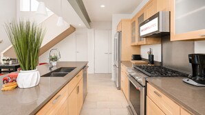 A modern kitchen with stainless steel appliances, wooden cabinets, and a large window providing natural light. - Modern Penthouse on Mass By CozySuites (Indianapolis)