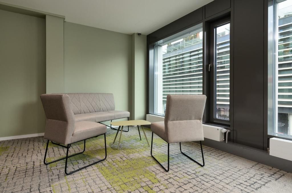 Ein Zimmer mit einer Couch, zwei Stühlen, einem kleinen Tisch und einem Fenster mit Jalousien.