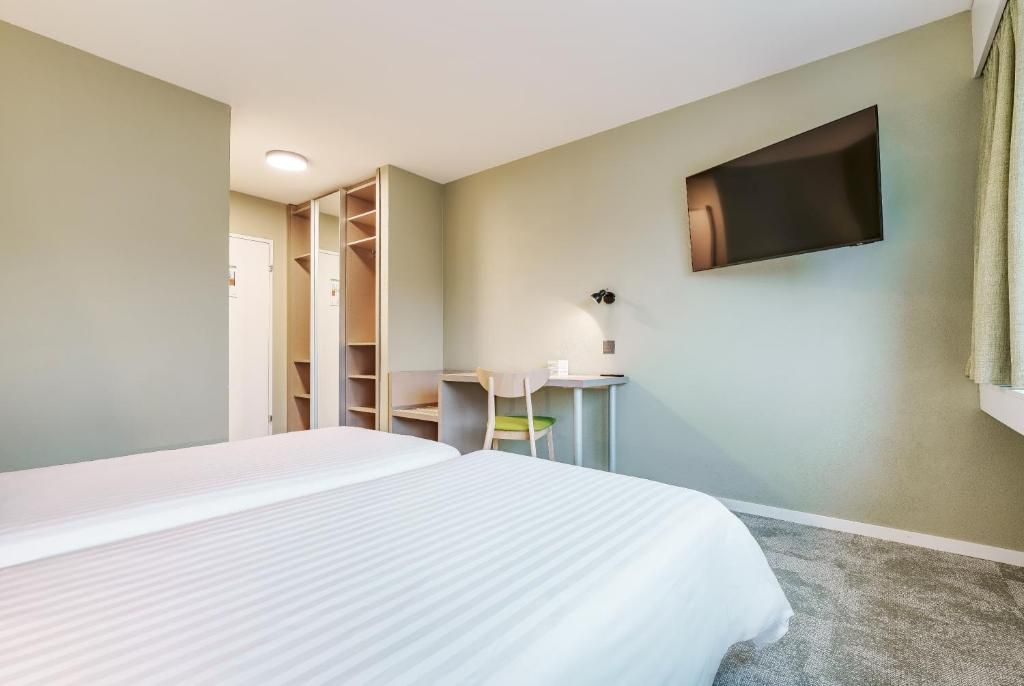 A hotel room with a bed, a desk, a chair, a TV, and a closet.