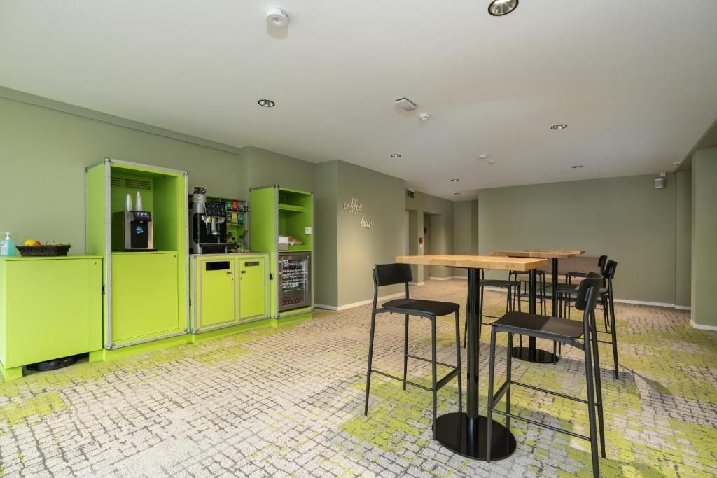 A room with a green kitchen area, a wooden table with chairs, and a patterned floor.