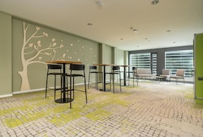 A modern interior with high ceilings, a patterned carpet, and a seating area with tables and chairs. -  flexy.motel Wil (Wil)