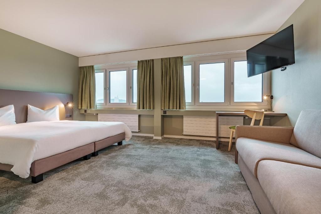 Een hotelkamer met een bed, een bureau, een stoel en een aan de muur bevestigde televisie.