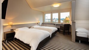 A hotel room with two beds, a desk, a chair, a lamp, and a window with a view of buildings. -  flexy.motel Wil (Wil)