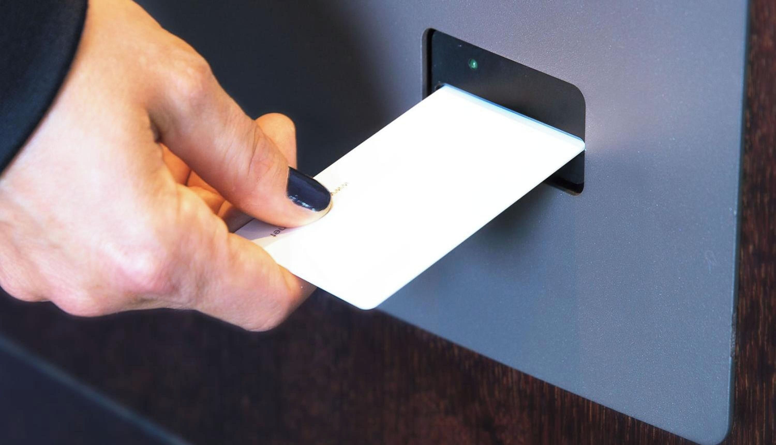 A hand holding a card against a wall-mounted device.