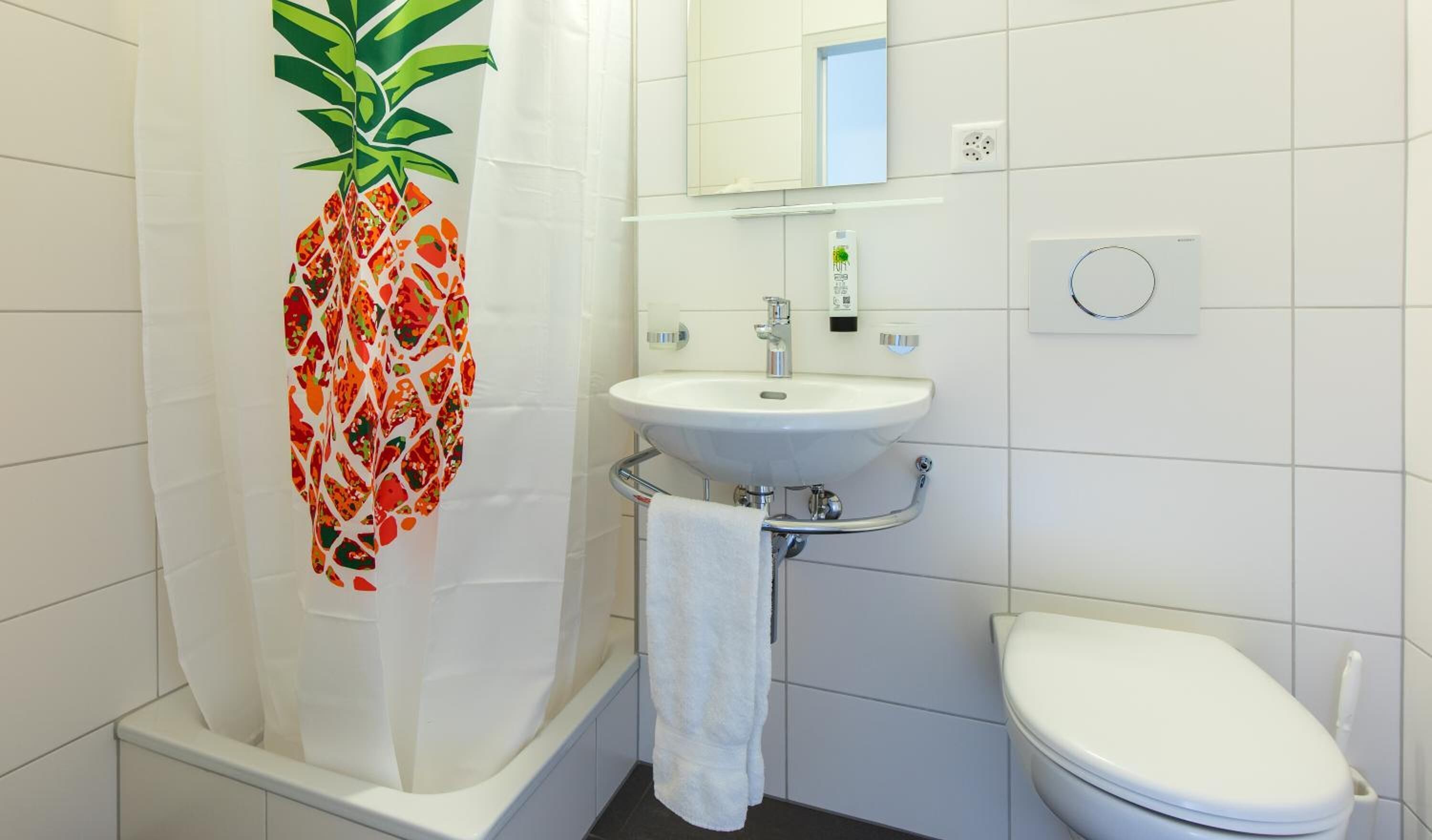 A bathroom with a white sink, a toilet, and a shower with a pineapple-themed shower curtain.