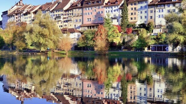 A row of multi-story buildings with balconies, reflecting in a calm body of water. -  flexy.motel Wil (Wil)
