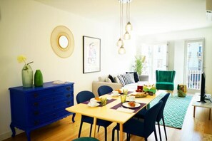 Un coin repas avec une table en bois dressée pour un repas, des chaises bleues, une commode bleue, une chaise verte et un tapis vert.