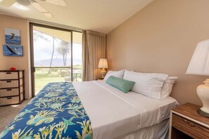 Een hotelkamer met een bed, een nachtkastje, een lamp, een raam met gordijnen, uitzicht op de omgeving en een muur met twee ingelijste foto's.