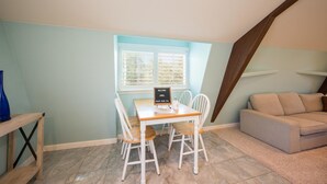 Een eetgedeelte met een tafel, stoelen, een blauwe vaas, een bord en een bank in een kamer met lichtblauwe muren en een schuine plafond.