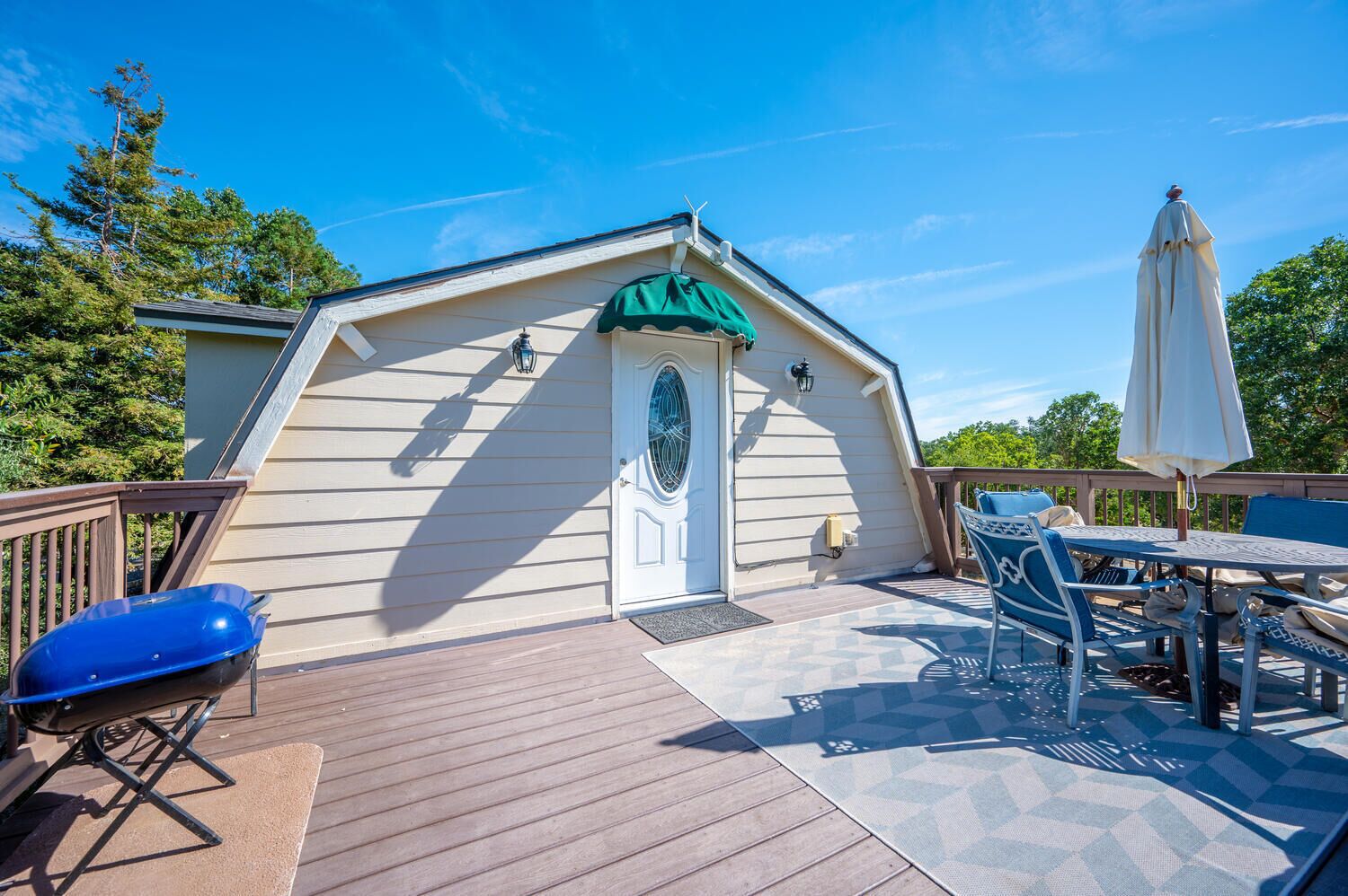 Une terrasse couverte avec un barbecue, une table et des chaises, et un parasol blanc.
