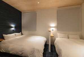 A hotel room with two beds, a dark accent wall, a standing lamp, and a ceiling light. - J-STAY Beppu indigo (Beppu)
