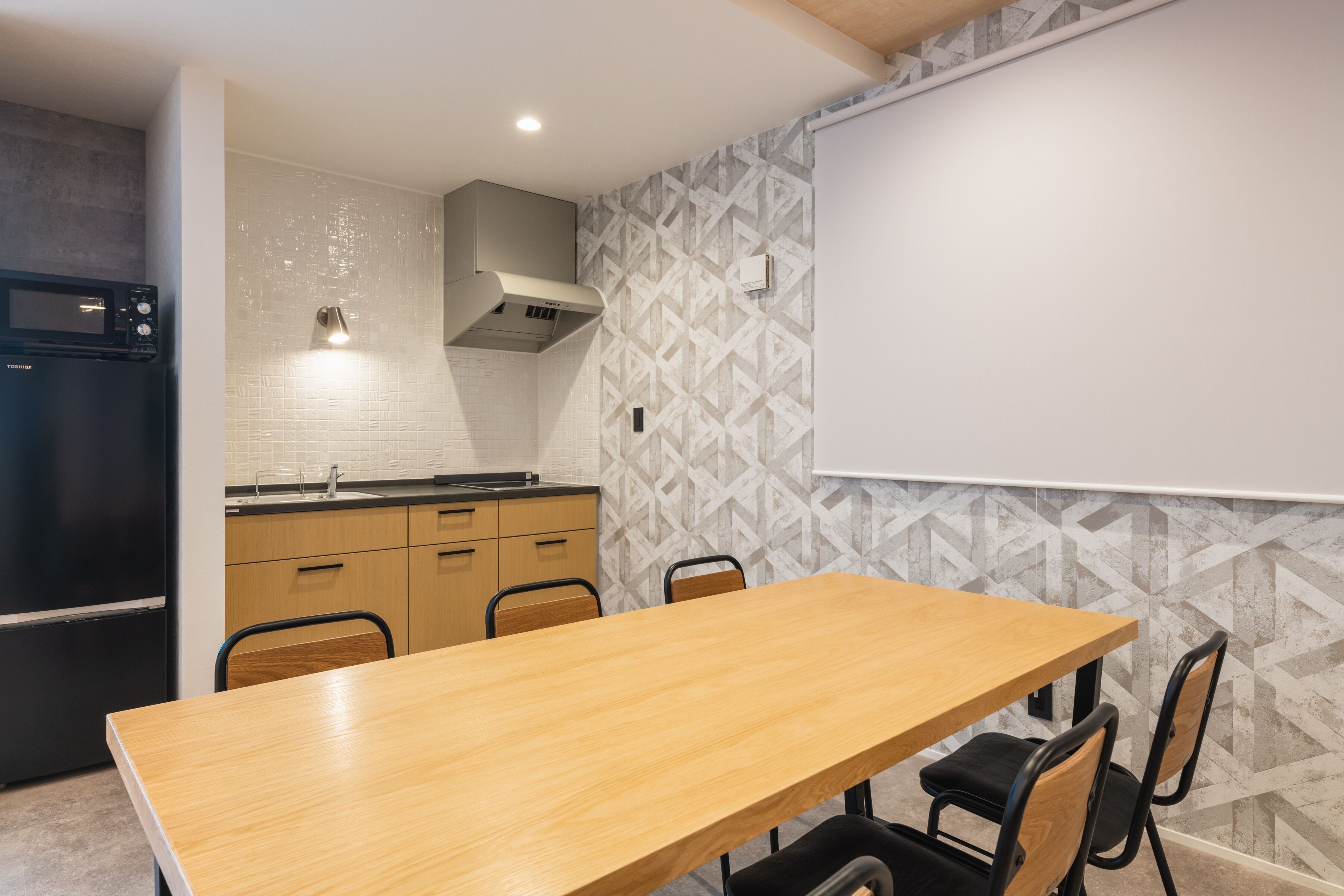 A modern kitchen with a wooden table and chairs, a black refrigerator, and a patterned backsplash.