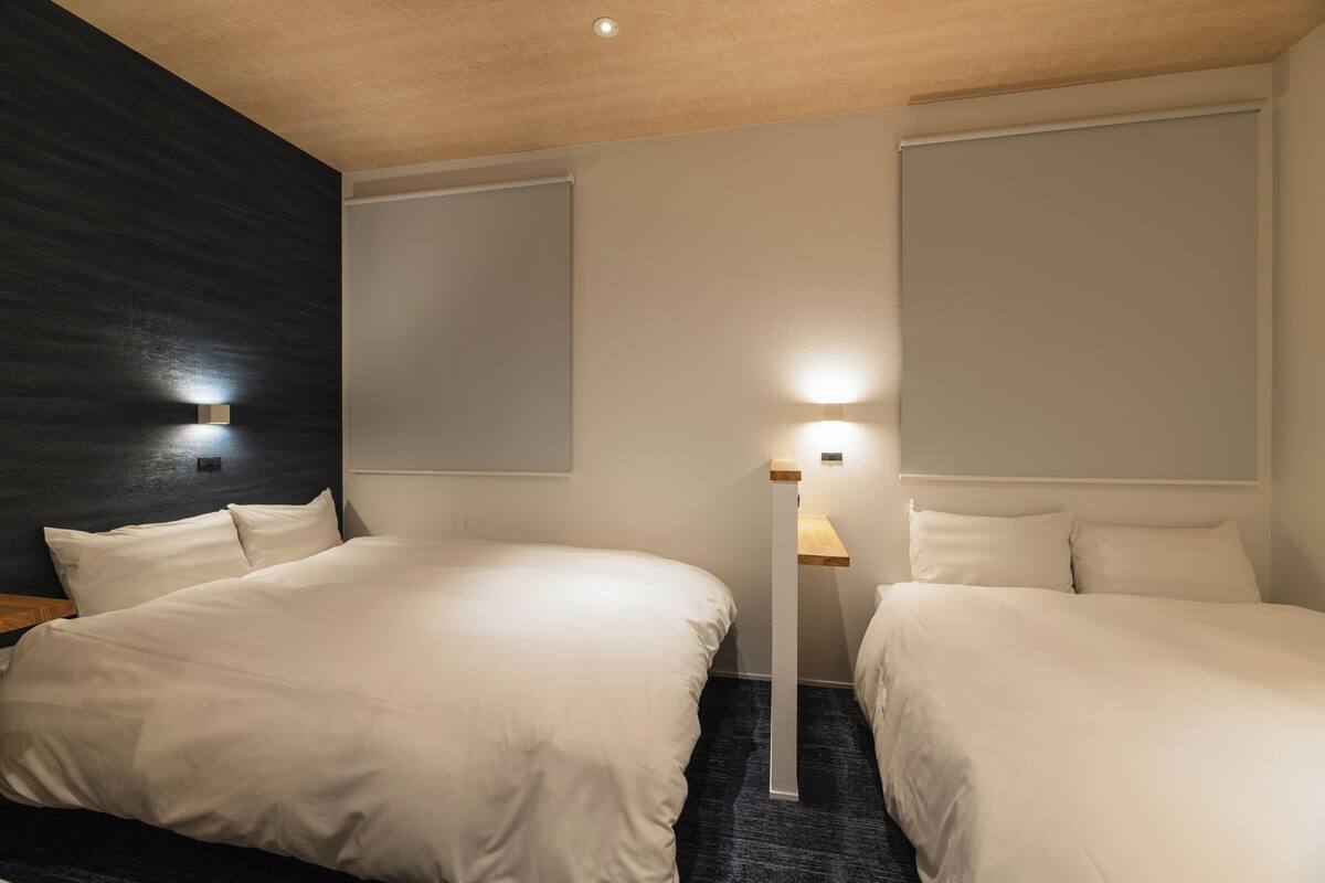 A hotel room with two beds, a dark accent wall, a standing lamp, and a ceiling light.