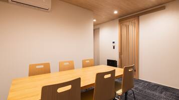 Una sala de conferencias con una mesa y sillas de madera, un equipo de aire acondicionado y una puerta con persianas verticales.