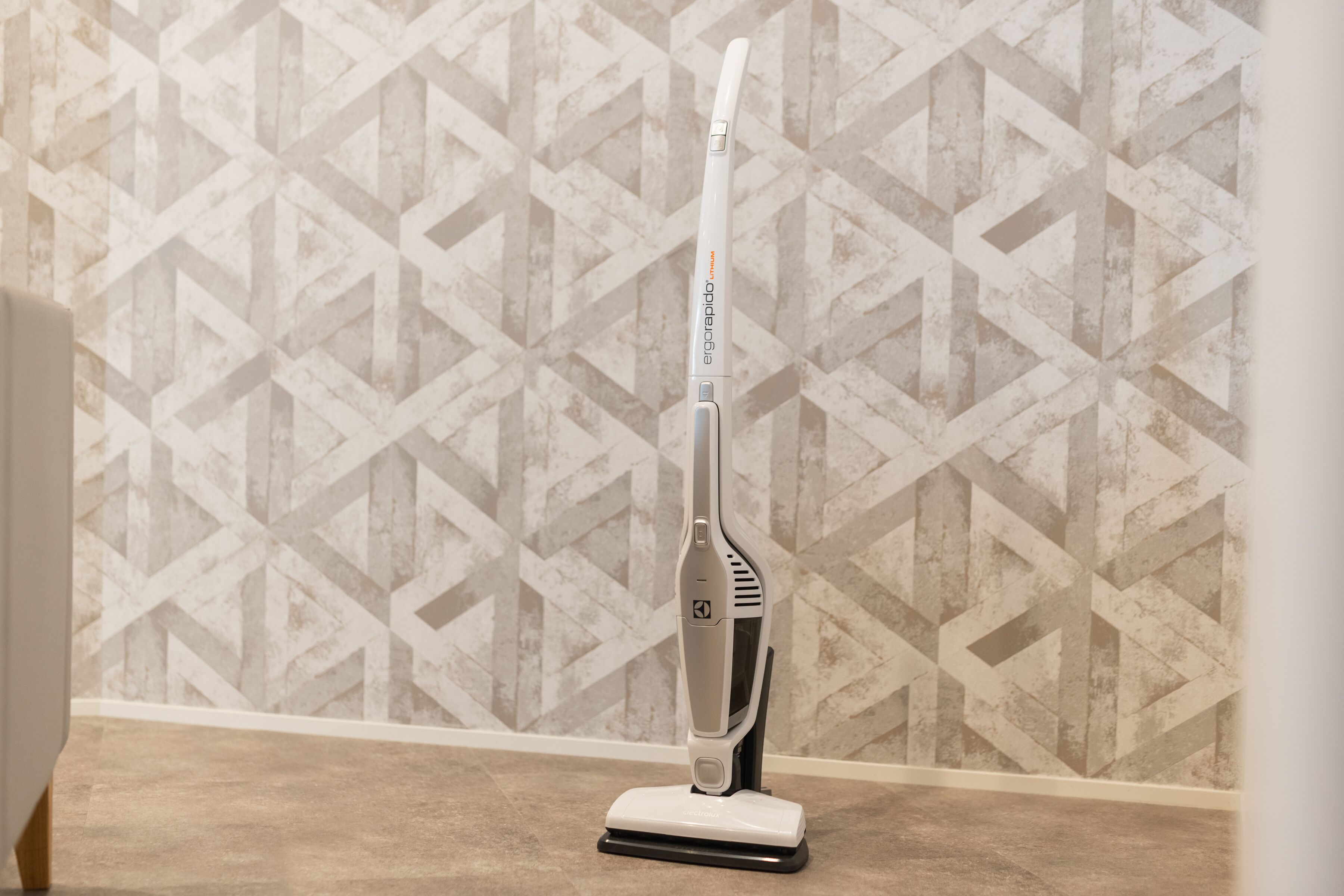 A vacuum cleaner on a carpeted floor with a patterned wall in the background.
