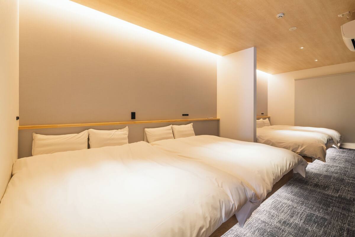 A hotel room with two beds, a wooden headboard, a grey carpet, and a modern ceiling design.