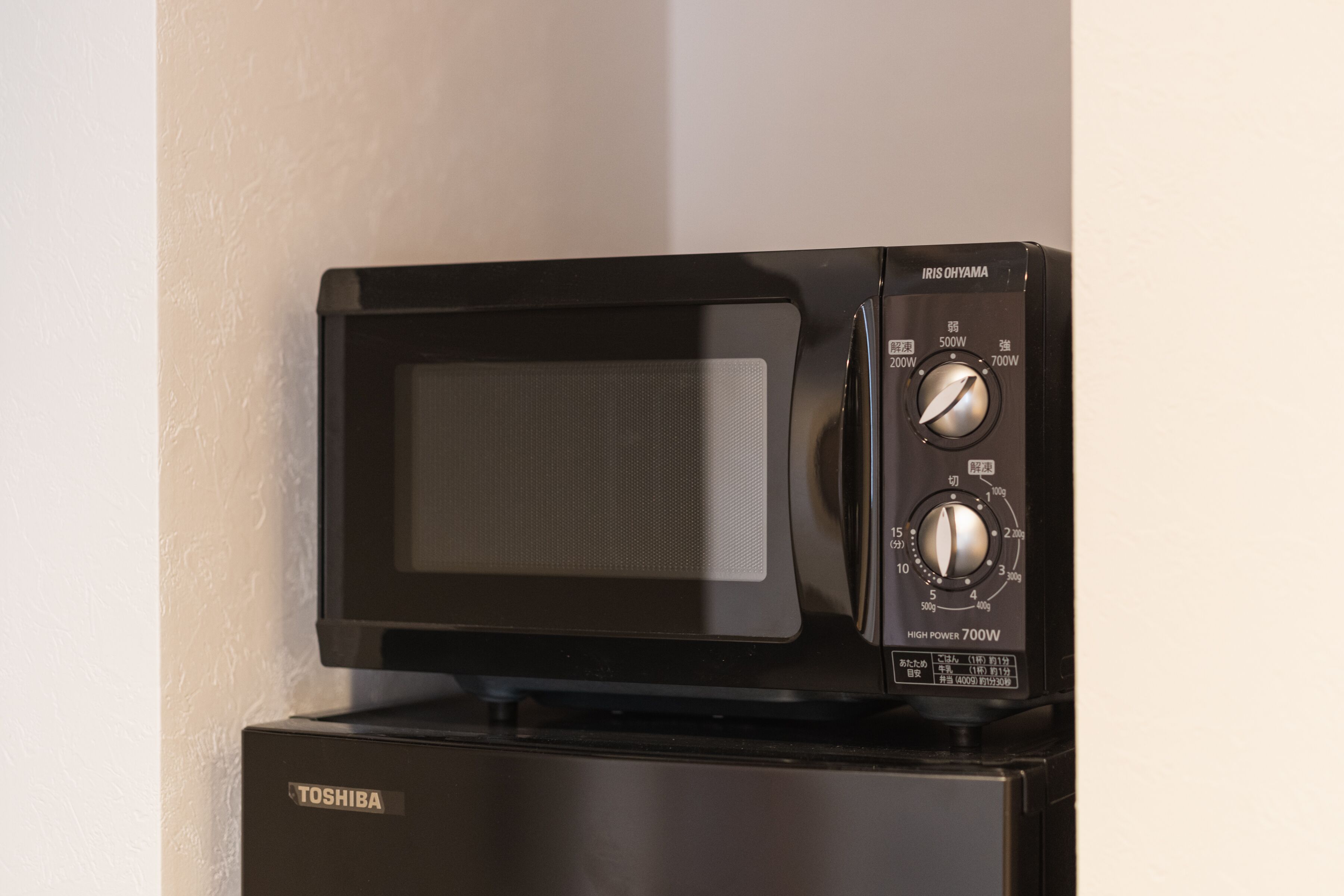 A Toshiba microwave oven with a digital display and control knobs, placed on top of a Toshiba refrigerator.