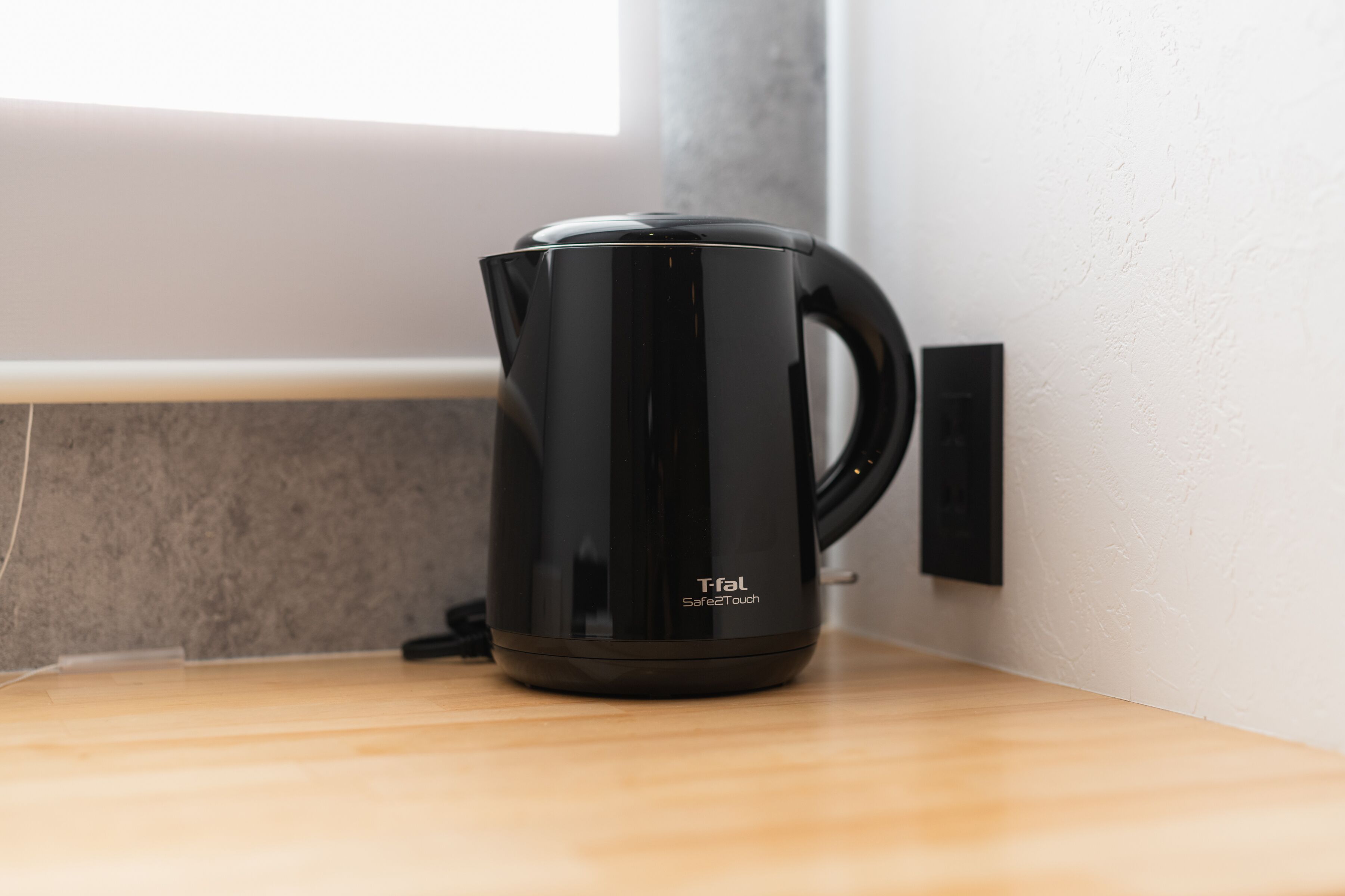 Una tetera Tefal SafeTouch negra sobre una encimera de madera cerca de una pared.