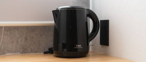 Una tetera Tefal SafeTouch negra sobre una encimera de madera cerca de una pared.