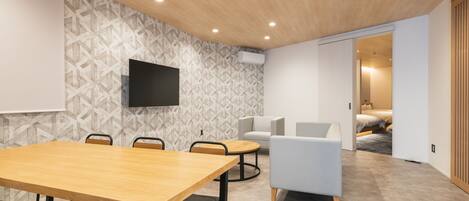 A modern conference room with a wooden table, chairs, a flat-screen TV, and a patterned wall.