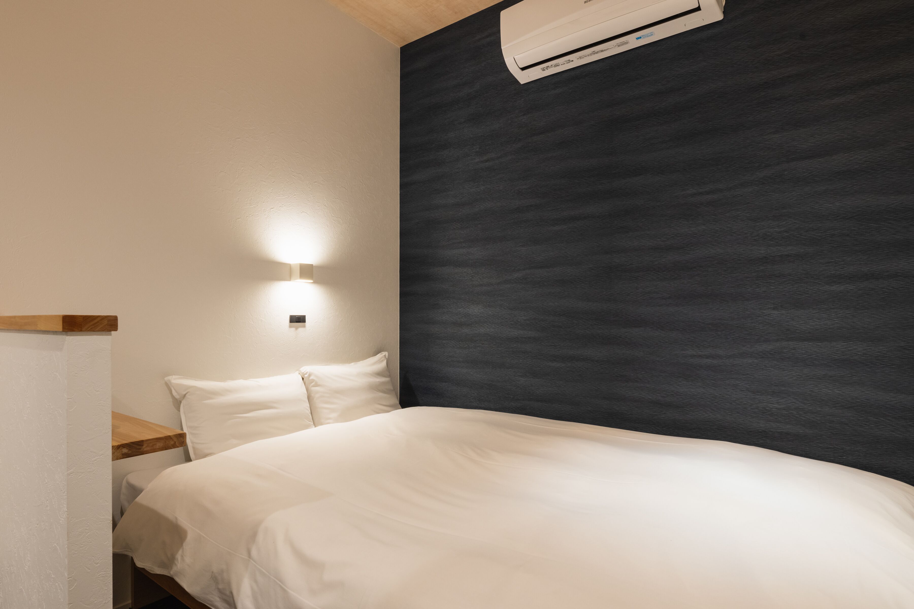 A bedroom with a bed, a nightstand, a wall-mounted air conditioner, and a wall light.