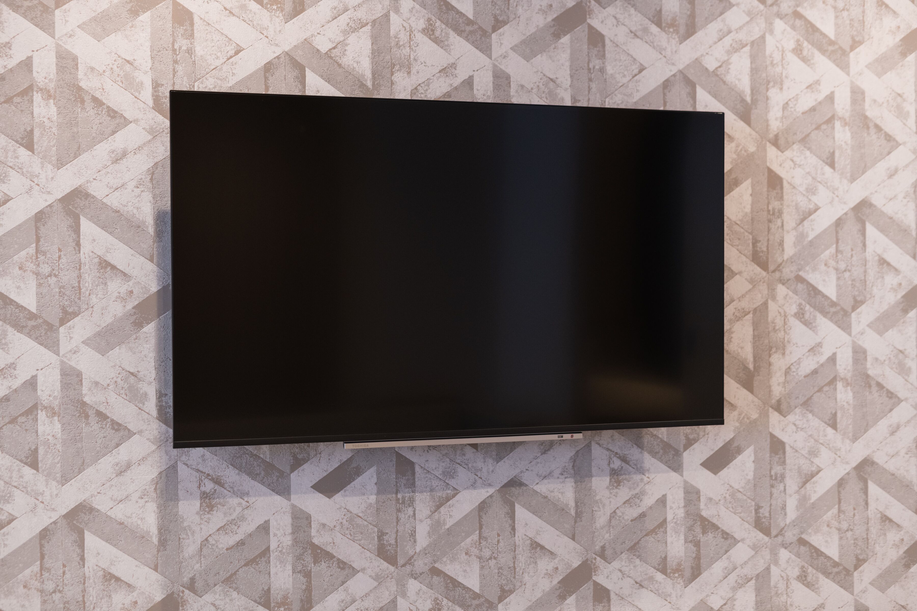 Un téléviseur à écran plat fixé au mur, avec un papier peint à motifs géométriques.
