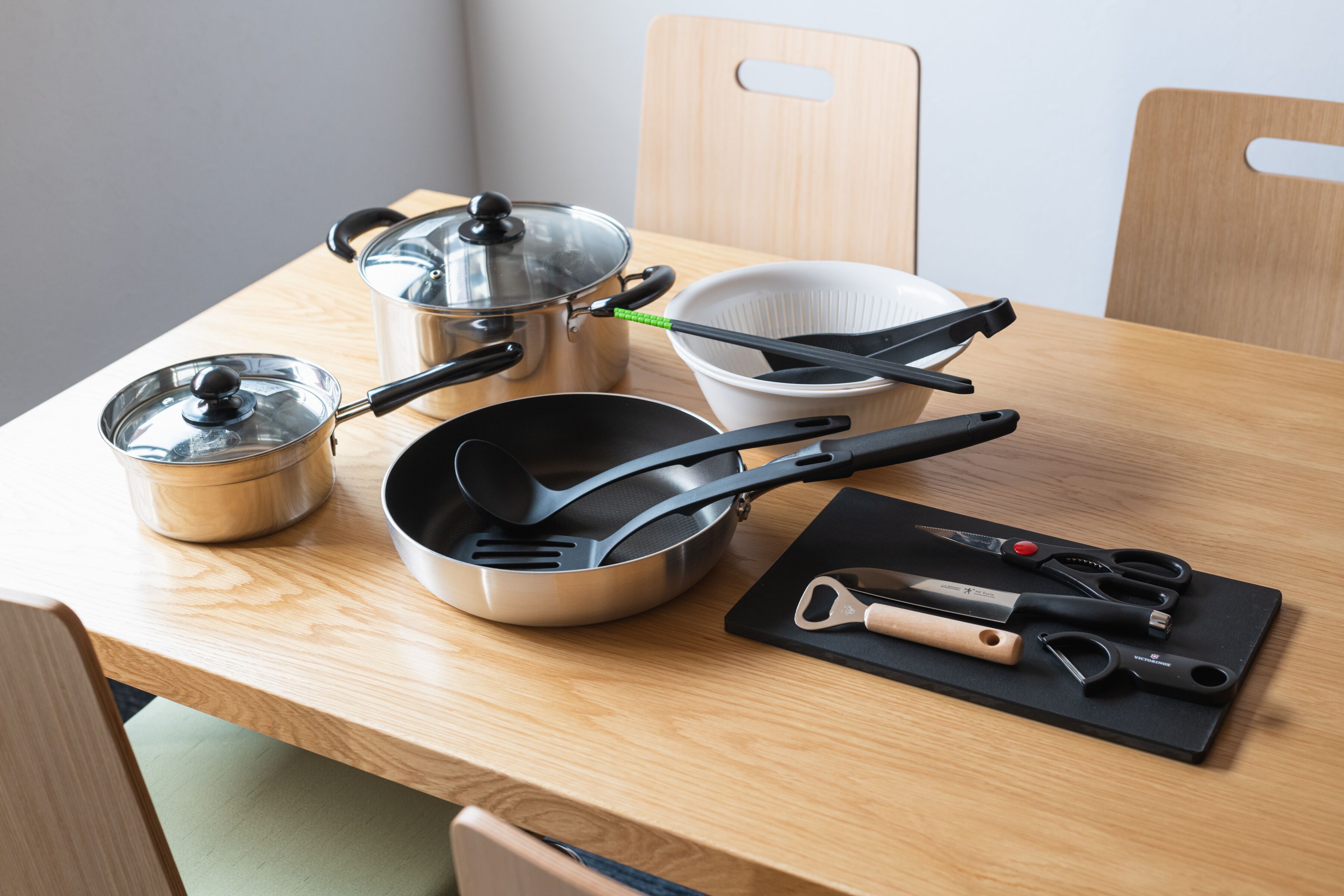 A kitchen counter with stainless steel cookware, a colander, and a cutting board with utensils.