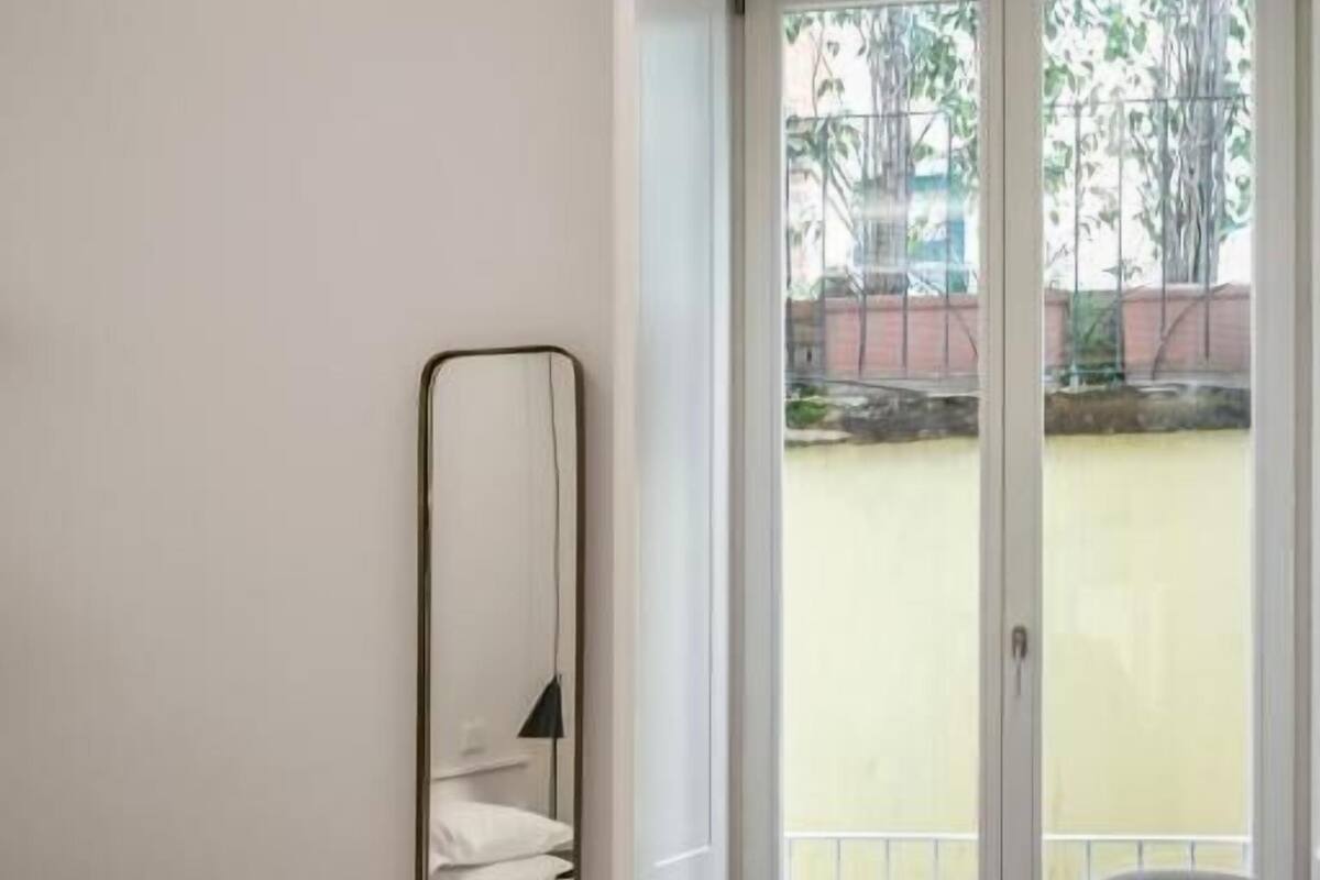 Ein Schlafzimmer mit einem großen Bett, einer flauschigen Decke, einem Sessel, einem Spiegel und einer Glasschiebetür, die auf einen Balkon führt.