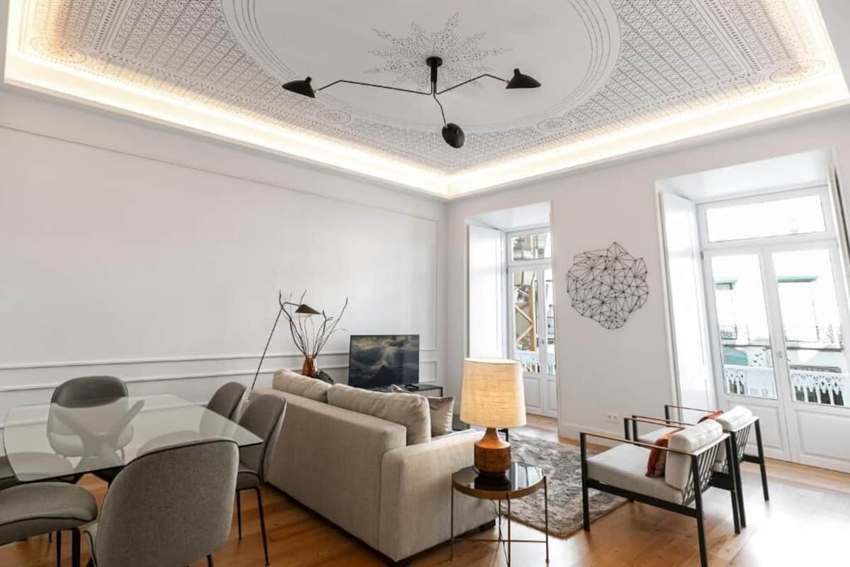 Ein modernes Wohnzimmer mit einer Couch, Sesseln, einem Glastisch, einer Lampe und einem geometrischen Wandbild.